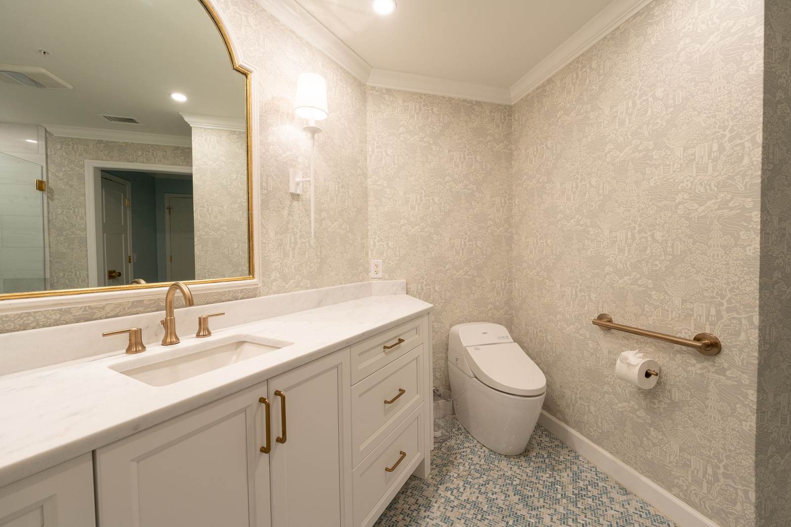 Toilet with a brass grab bar on the side wall beside a white vanity