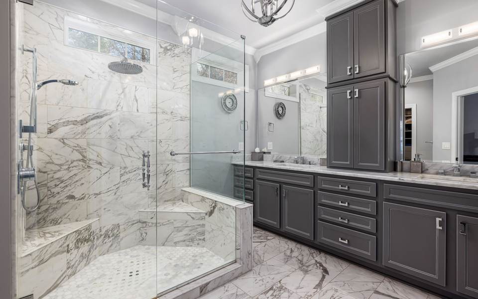 Marble-look walk-in shower with a tiled bench and glass walls beside a gray double vanity