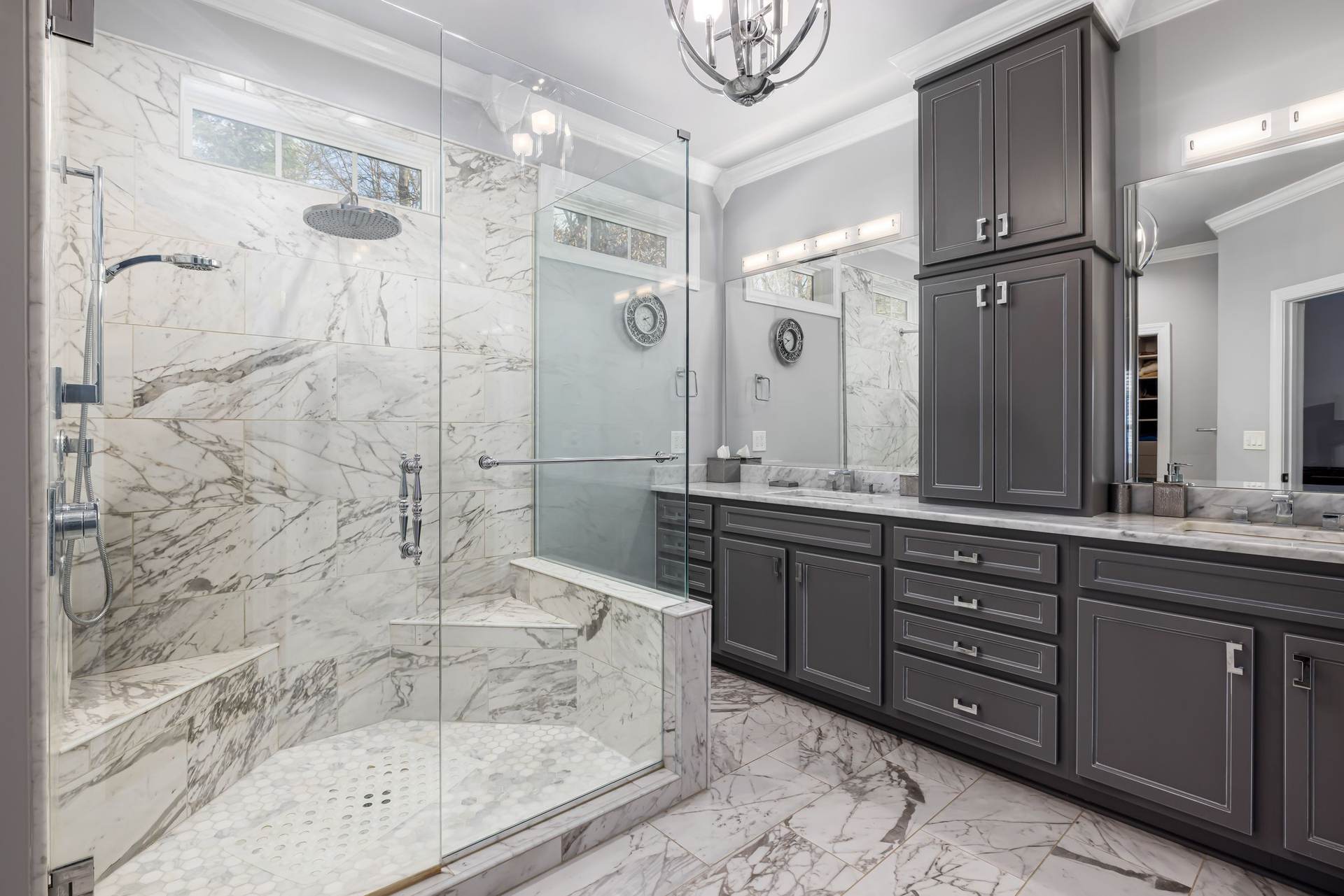 Bathroom with a large glass shower, a built-in bench, marble-look tile, and a dark double vanity