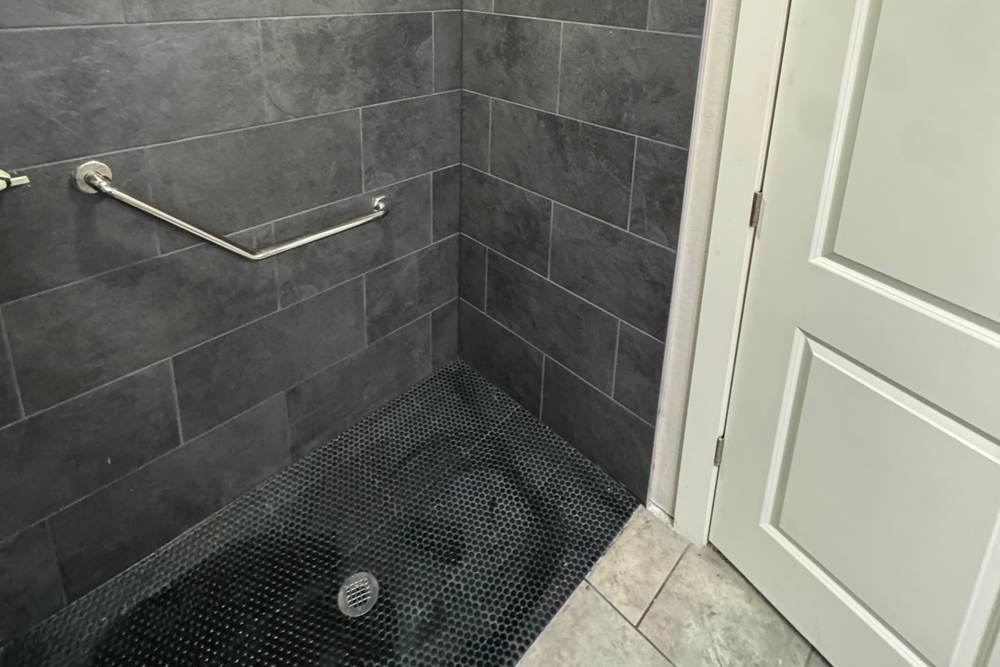Low entry of a tiled walk-in shower with a black hex floor and a grab bar, in a Bixby home we remodeled