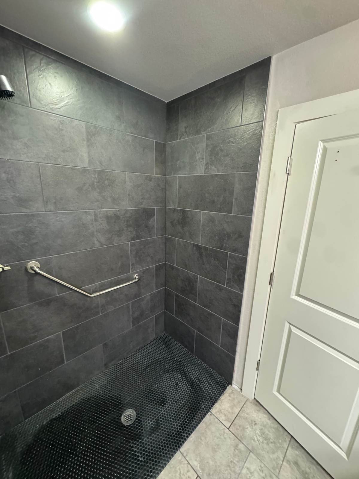 The low entry of the Bixby walk-in shower, with a black hex floor and a grab bar