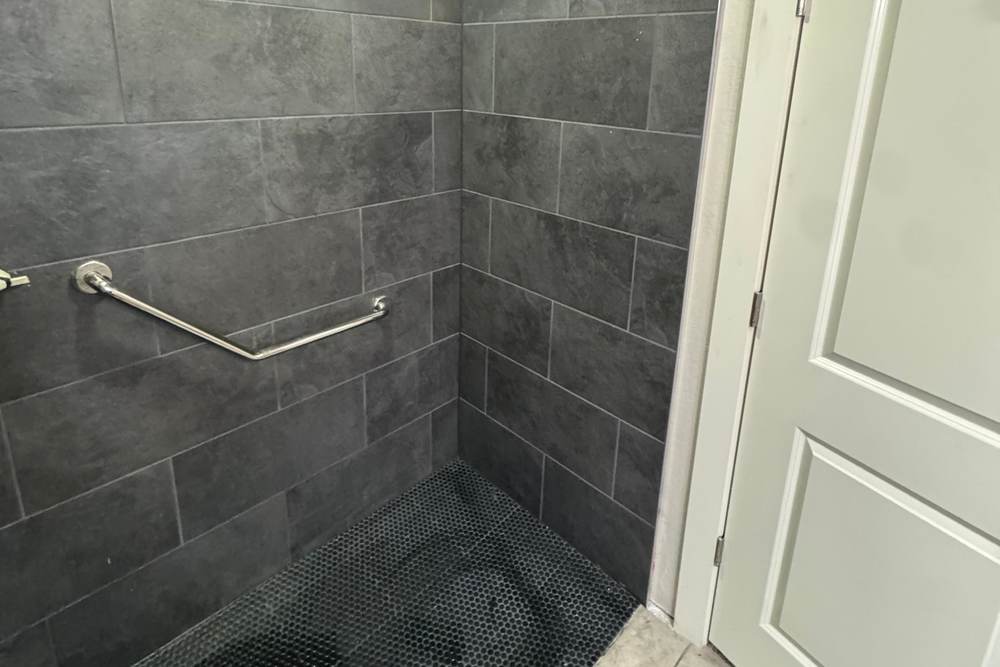 Low entry of a tiled walk-in shower with a black hex floor and a grab bar, in a Bixby home where we opened the slab at the drain
