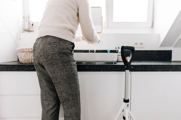 Older woman with a rollator walker washing her hands at a bathroom sink