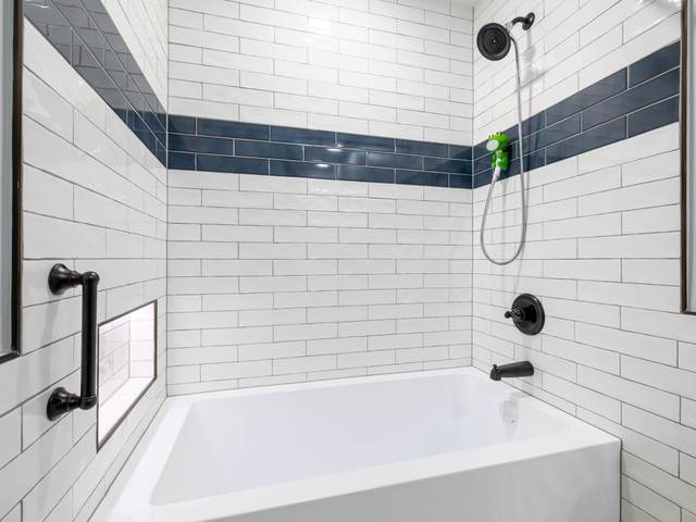 Alcove bathtub with white subway tile, a navy tile band, a niche, and a black grab bar