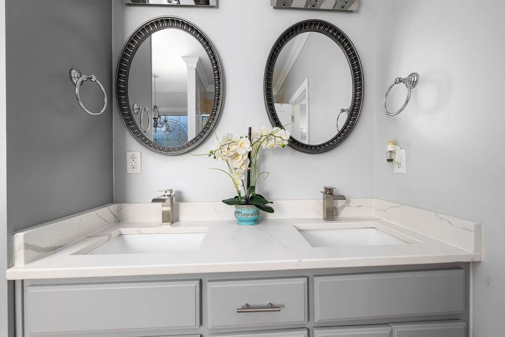 Painted gray double vanity with a new quartz top, two undermount sinks, brushed nickel faucets and oval mirrors