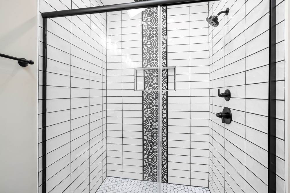 White subway tile shower with dark grout lines, a patterned tile stripe, a recessed niche and matte black fixtures