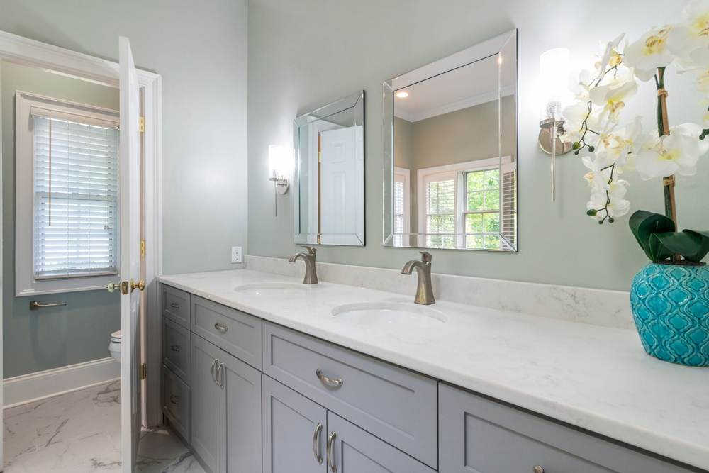 Gray double vanity with a wall sconce beside each mirror at face height and an outlet beside the sink