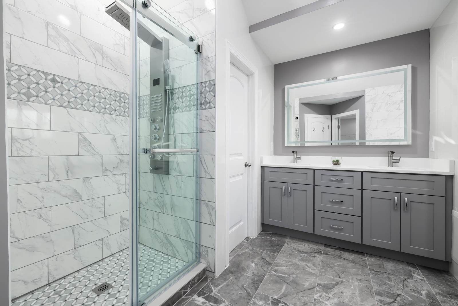 Remodeled bathroom with a glass walk-in shower beside a gray double vanity