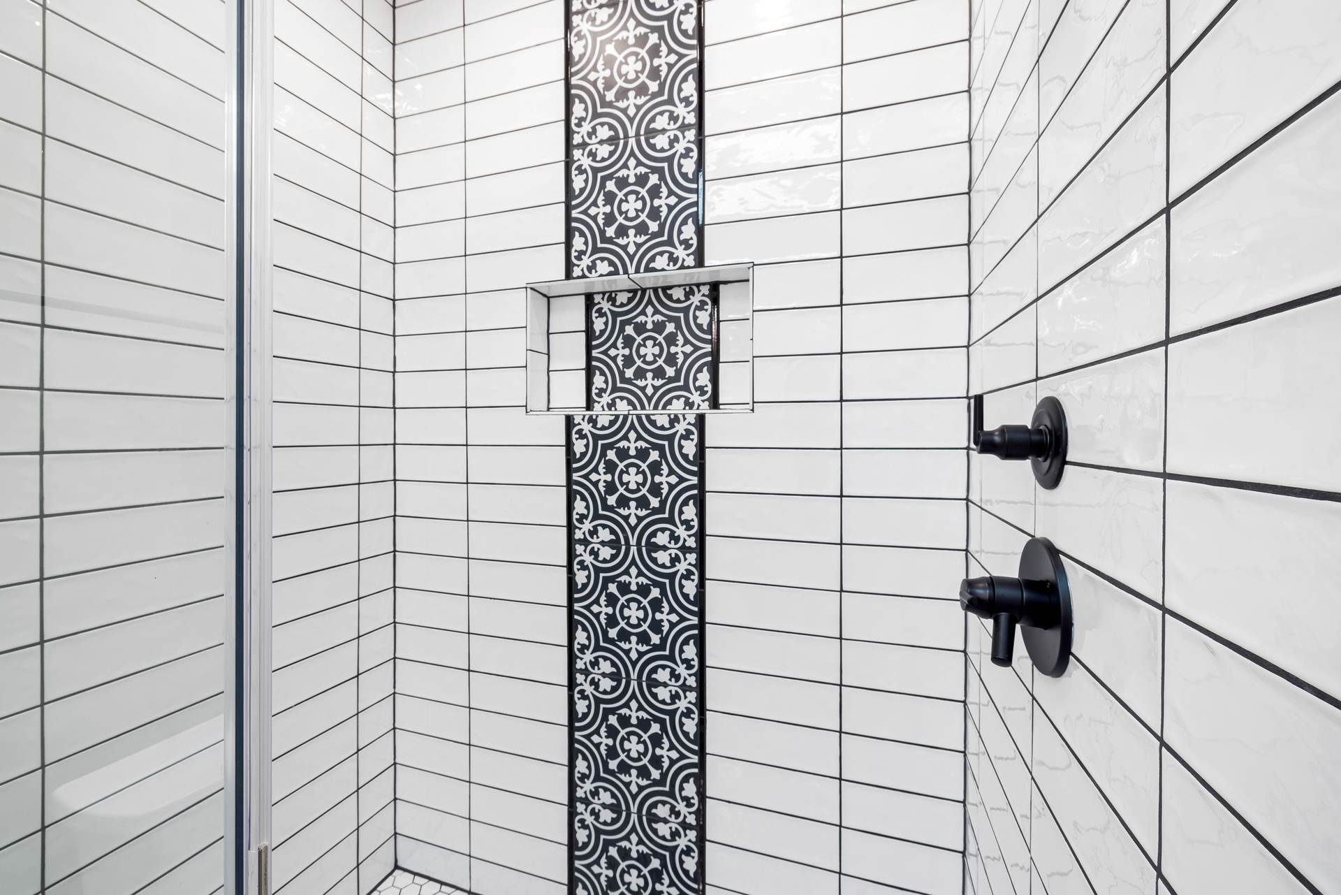 White tile shower with a patterned tile strip, a recessed niche and black fixtures