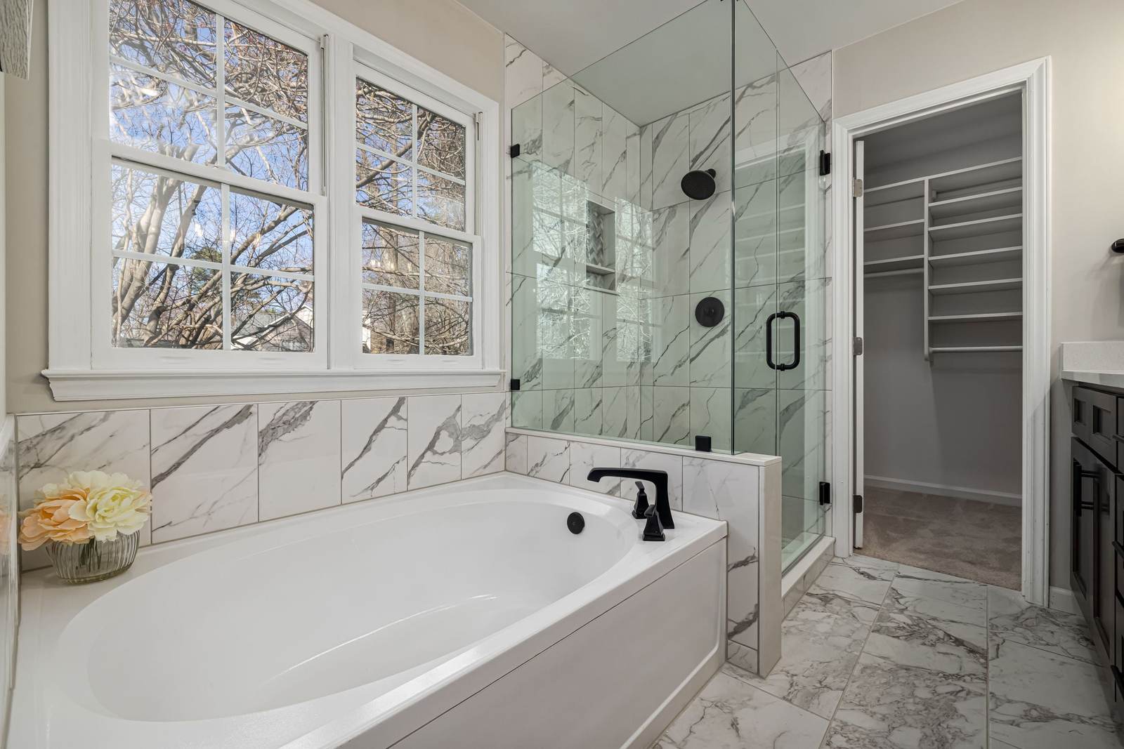 Primary bathroom with a drop-in tub under double windows, marble-look tile and a frameless glass corner shower with matte black fixtures