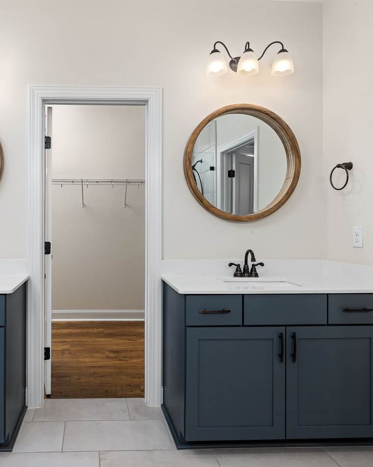 Two navy vanities with round wood mirrors, a light bar over each and an outlet beside each sink