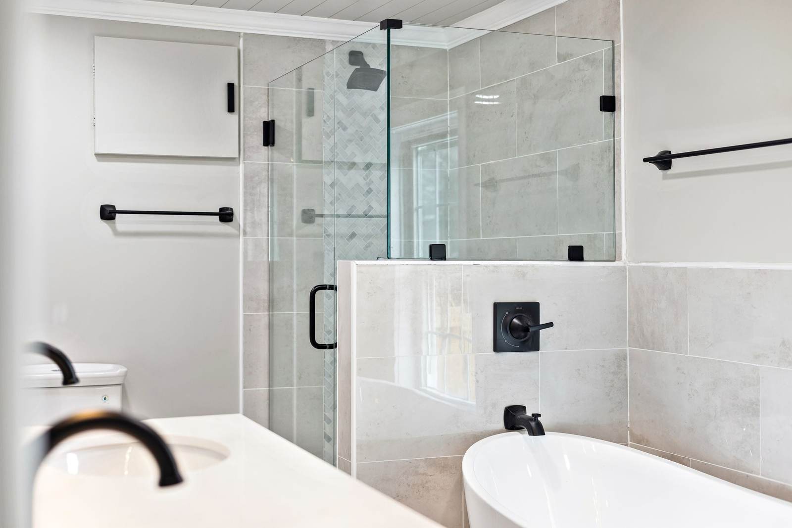 Primary bathroom with a freestanding tub in front of a tiled half wall and a frameless glass shower, with matte black fixtures