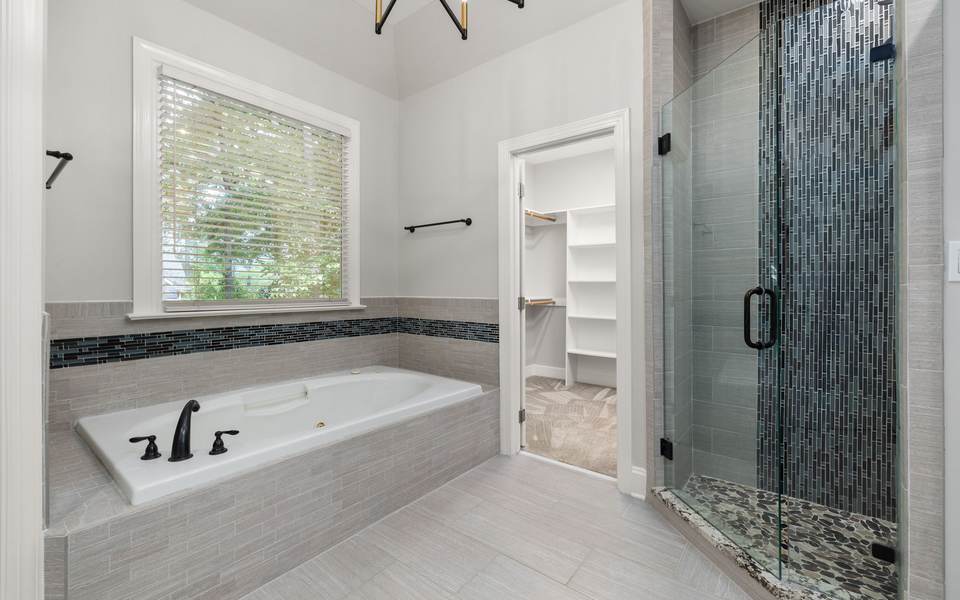 Bathroom with a tiled soaking tub under a window and a glass shower with a mosaic accent wall