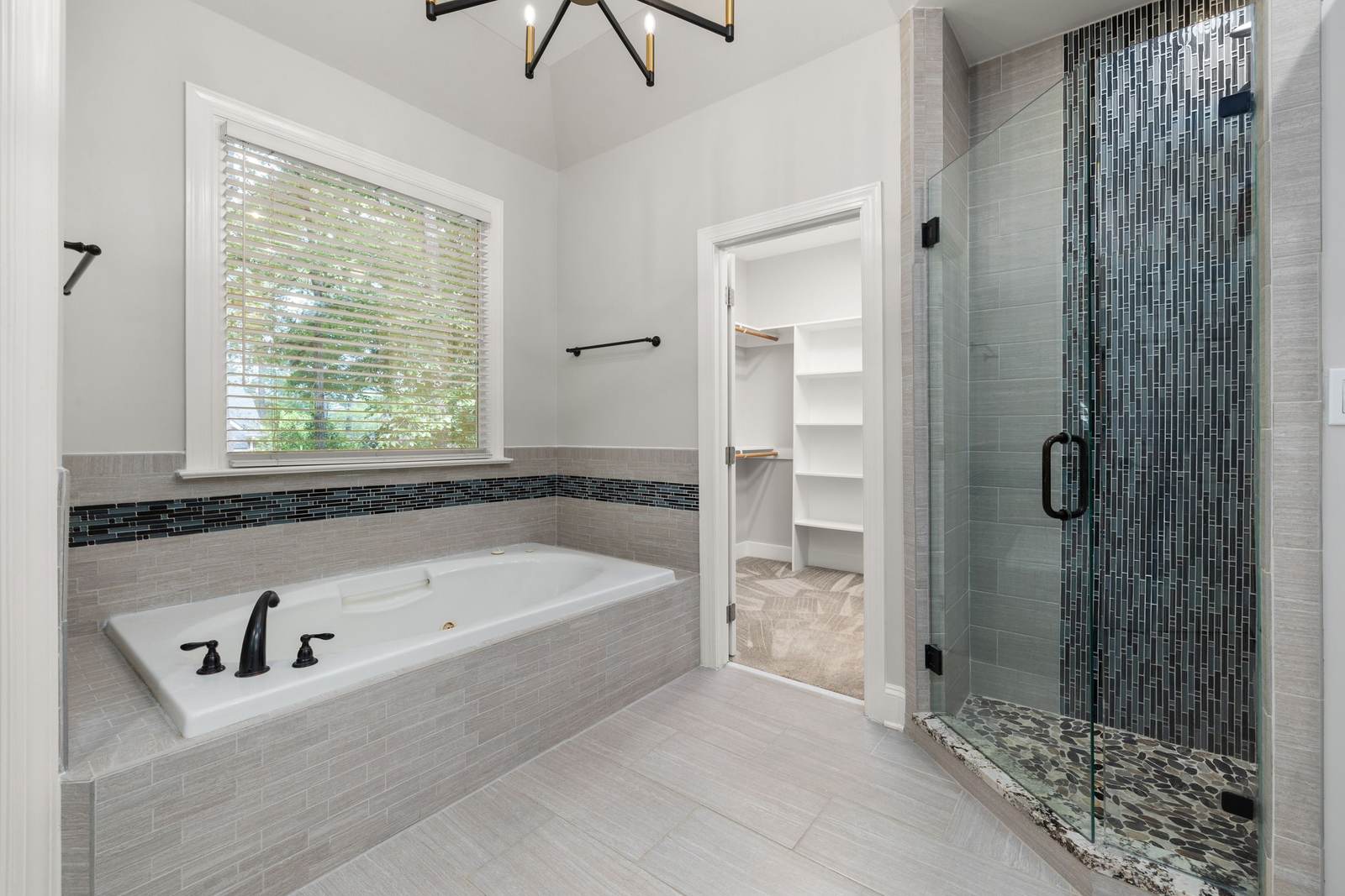 Primary bathroom with a drop-in soaking tub under a window and a frameless glass shower with a mosaic accent stripe