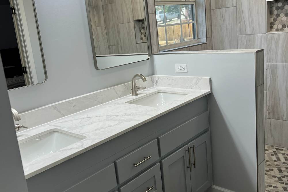 GFCI outlet on a new half wall beside a vanity sink, under a new four-light bar, in a master bathroom we remodeled in east Tulsa