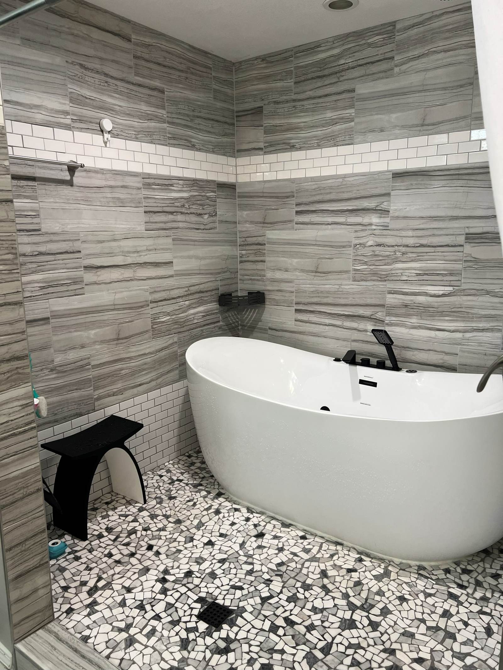 Freestanding tub and a black bench on a pebble floor, with a white subway tile band, in the south Tulsa wet room we built