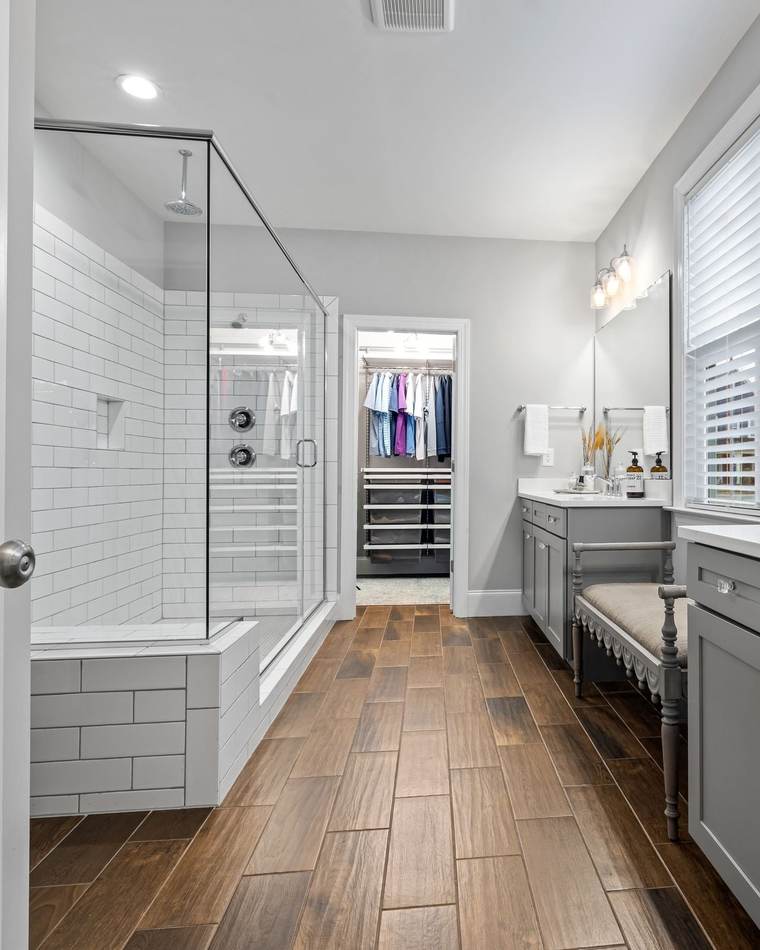 Long primary bathroom with a glass-enclosed subway tile shower, a gray double vanity and a wood-look tile floor