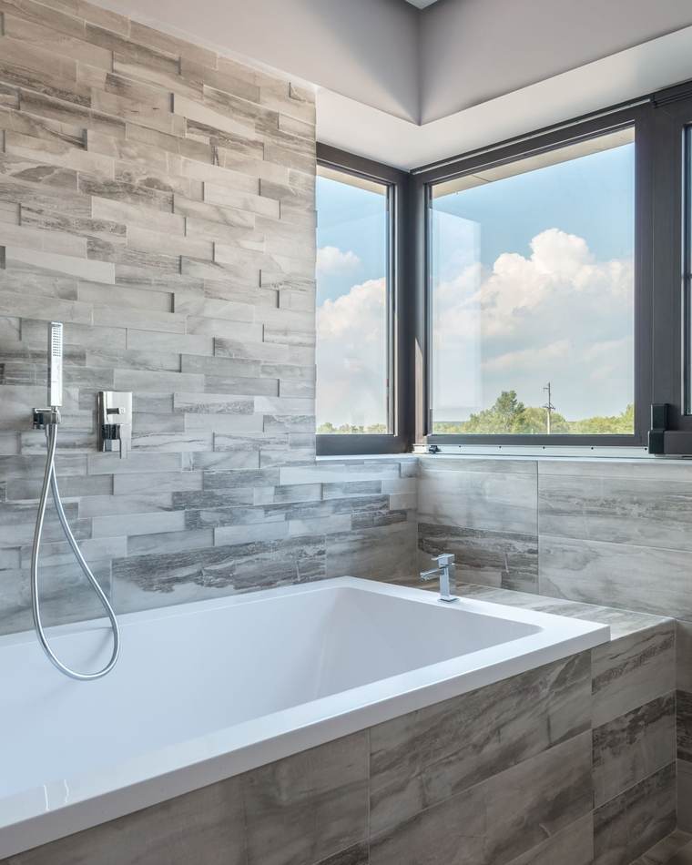 Tiled bathroom with a white soaking tub, a hand shower and corner windows looking out over trees and open sky