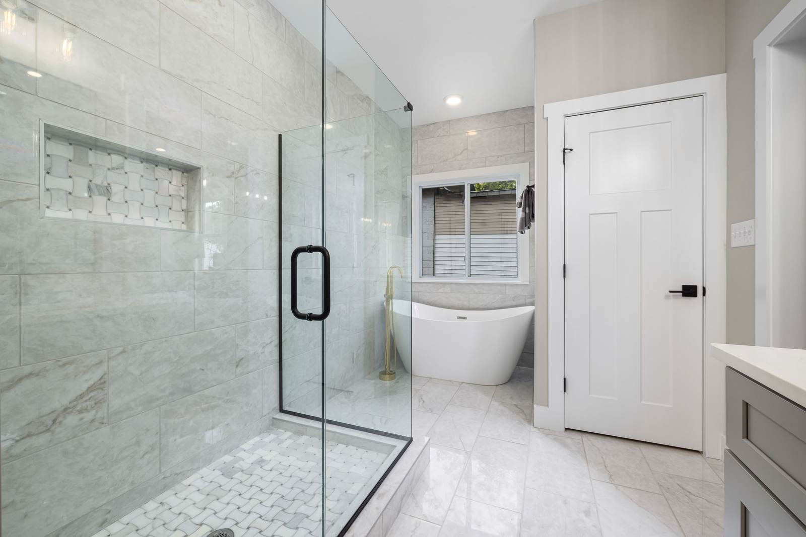Remodeled bathroom with a frameless glass walk-in shower, a tiled niche, and a freestanding tub