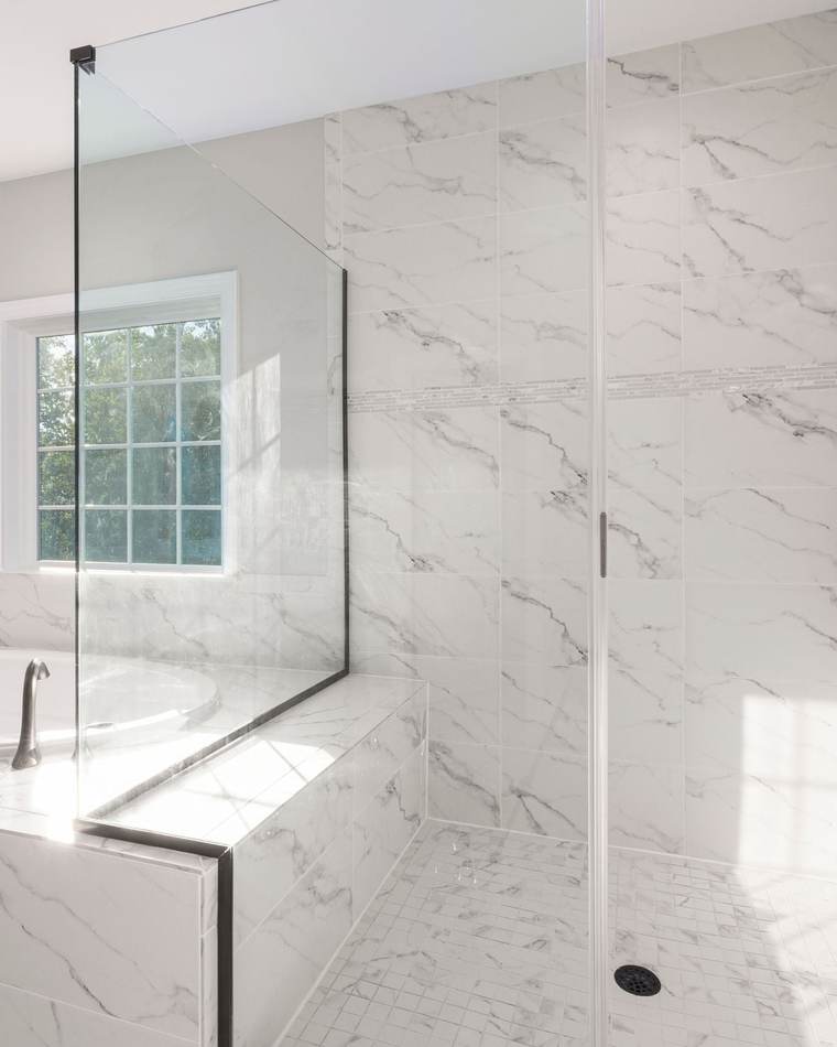 Bright bathroom with a frameless glass walk-in shower in marble-look tile beside a tiled drop-in tub, with matte black fixtures