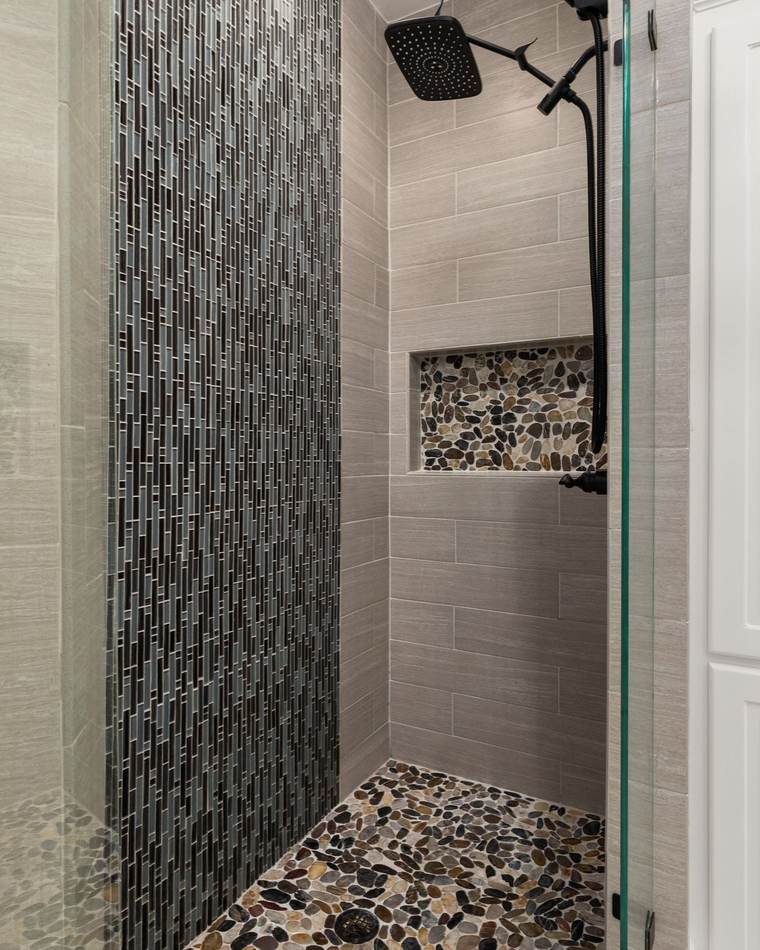 Tiled walk-in shower with a river pebble floor, a matching pebble niche, a glass mosaic stripe and a matte black rain head