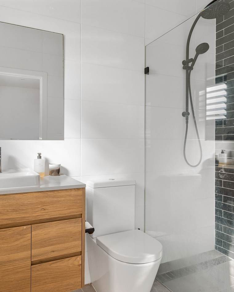 Bright bathroom with a wood vanity, a floor-mounted toilet and a glass walk-in shower with dark brick-pattern tile