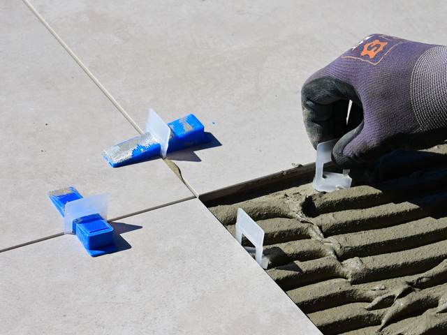 Gloved hand setting tile leveling clips between large gray floor tiles