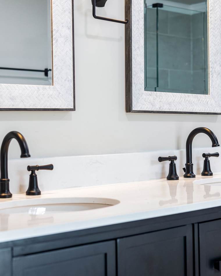 Dark double vanity with a white quartz top, two oval undermount sinks and matte black widespread faucets under framed mirrors