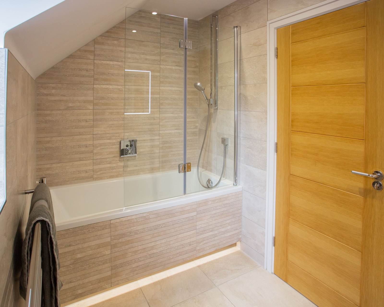 Tiled alcove tub with a folding glass bath screen and a hand shower on a slide bar