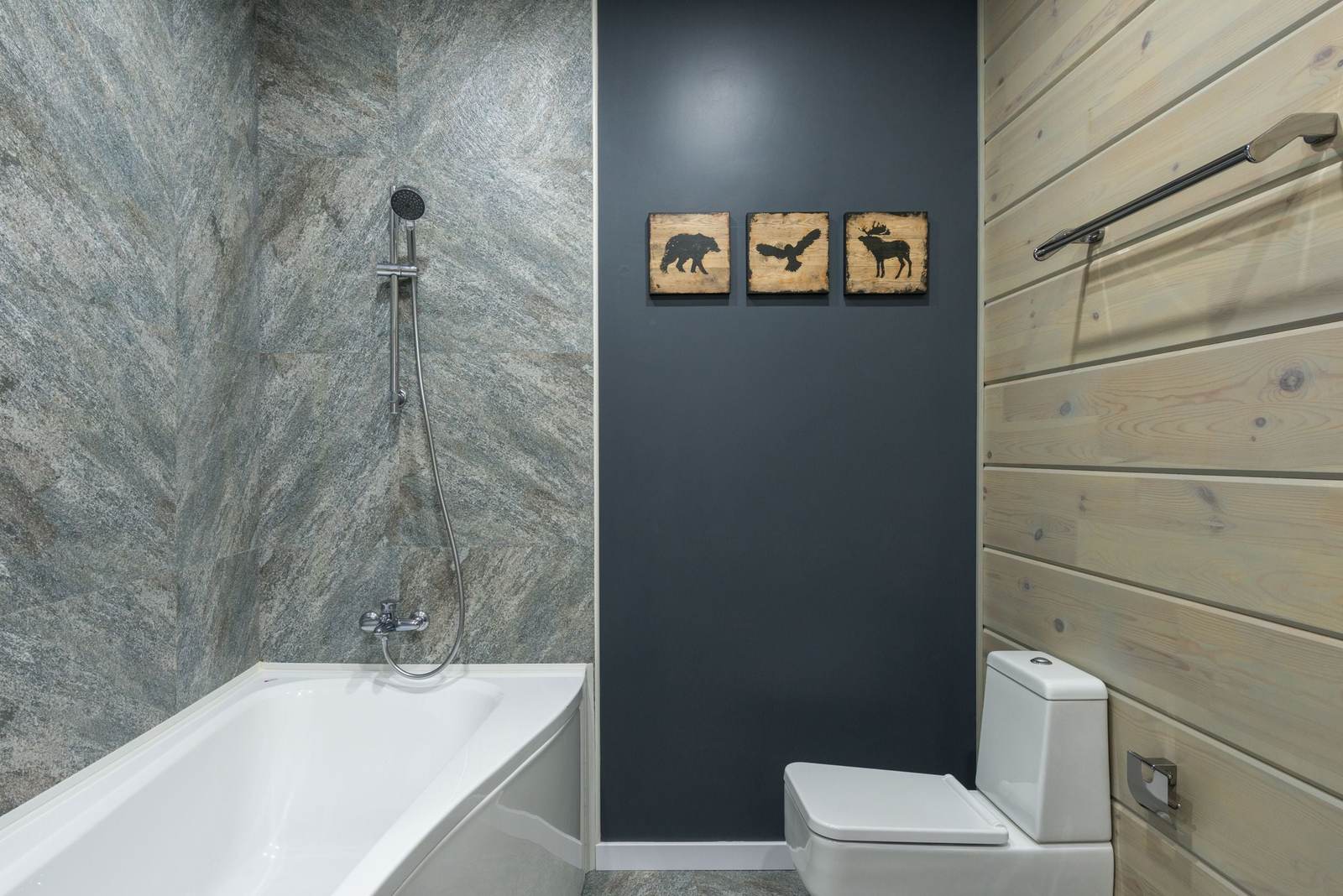 Bathtub with a hand shower on a slide bar against stone-look tile, beside a whitewashed wood plank wall and a toilet