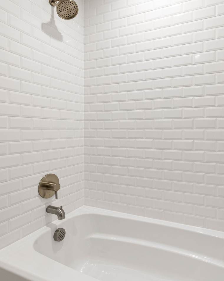 New white alcove bathtub set in beveled white subway tile, with a brushed nickel spout, shower valve and recessed niches