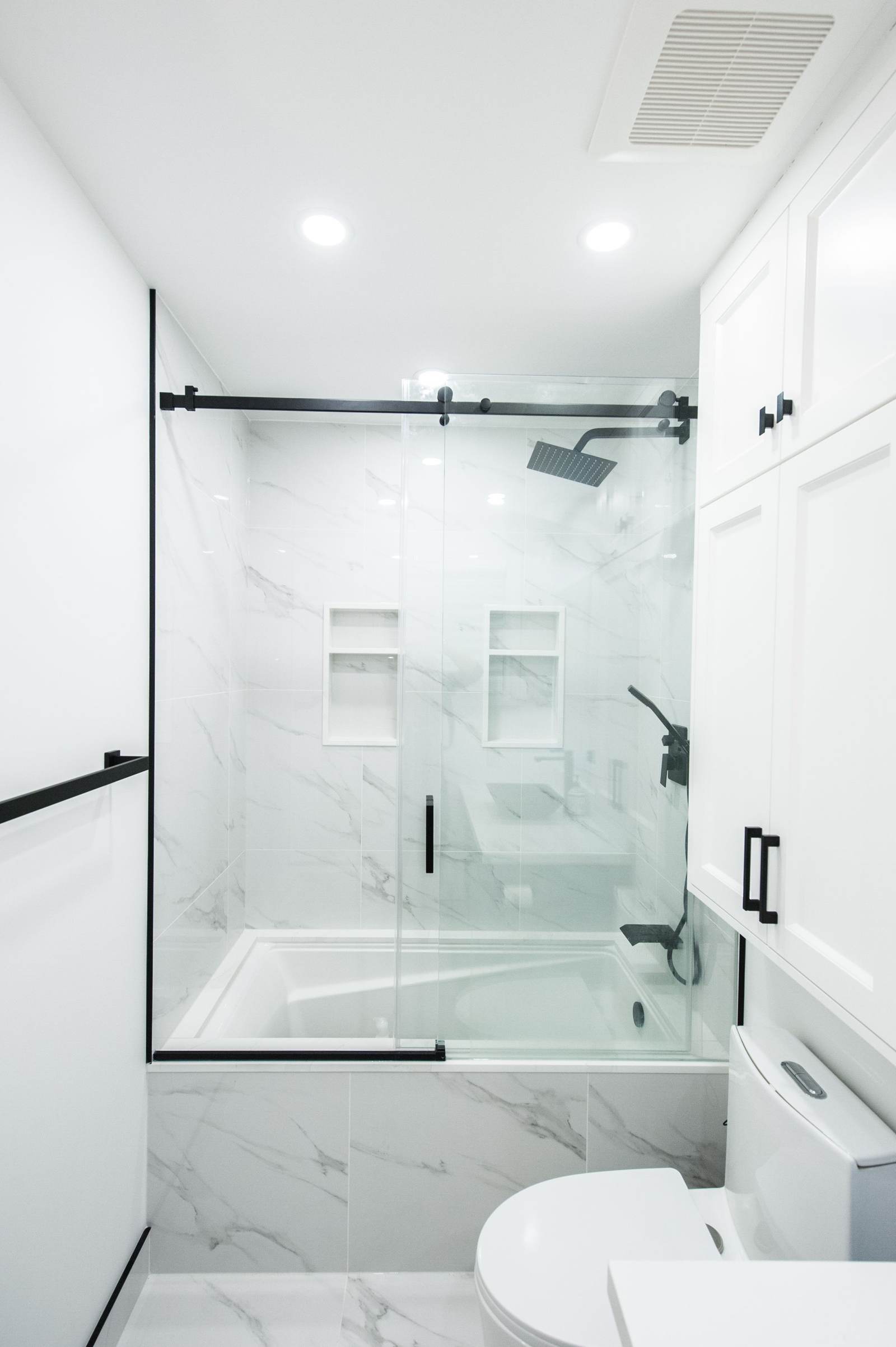 Tiled tub and shower with marble-look walls, two niches, a sliding glass door and matte black fixtures