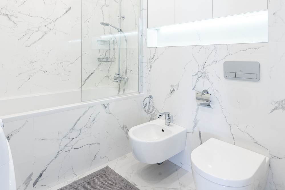Bidet installed beside a toilet in a bathroom with tiled walls