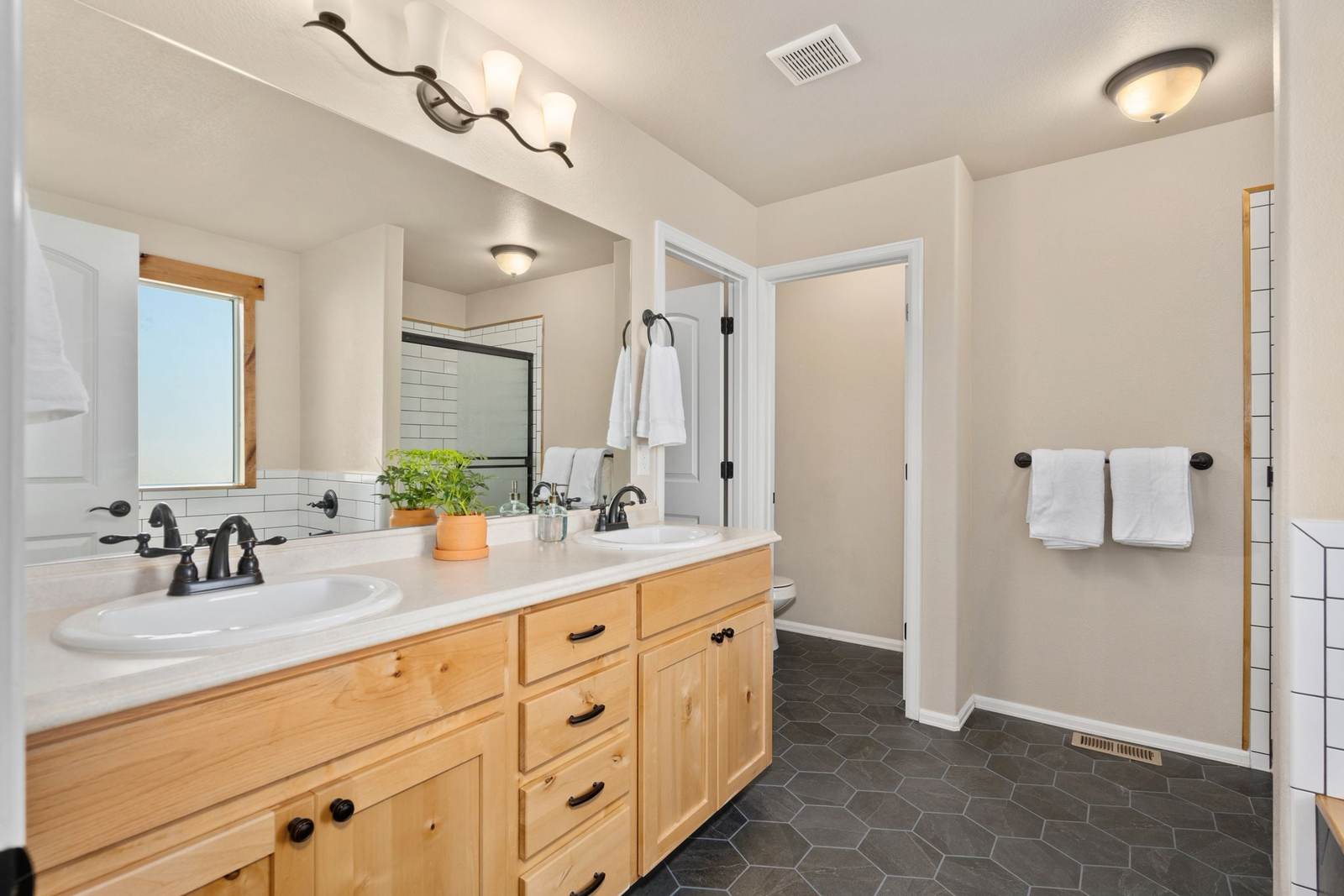 Knotty pine double vanity with a pale one-piece top, drop-in sinks and bronze faucets, the kind of builder vanity many houses still have