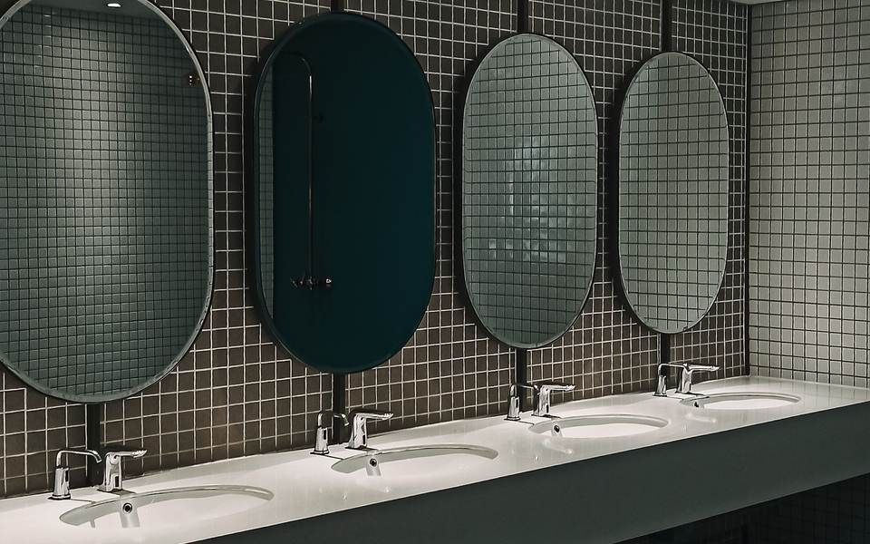 Commercial restroom with a long counter, a row of sinks and oval mirrors over dark mosaic tile