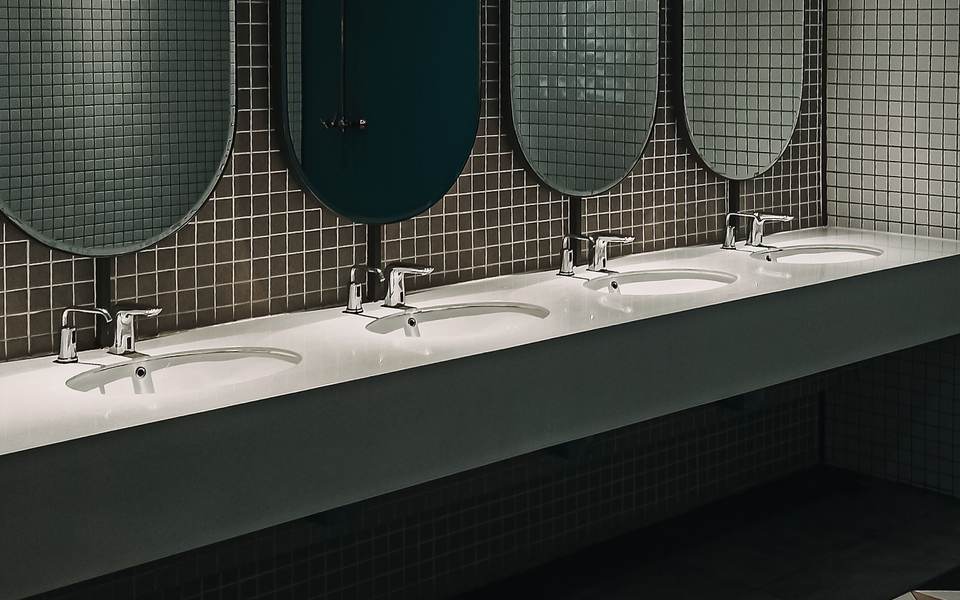 Commercial restroom with a row of oval mirrors over a long counter and a geometric tile floor