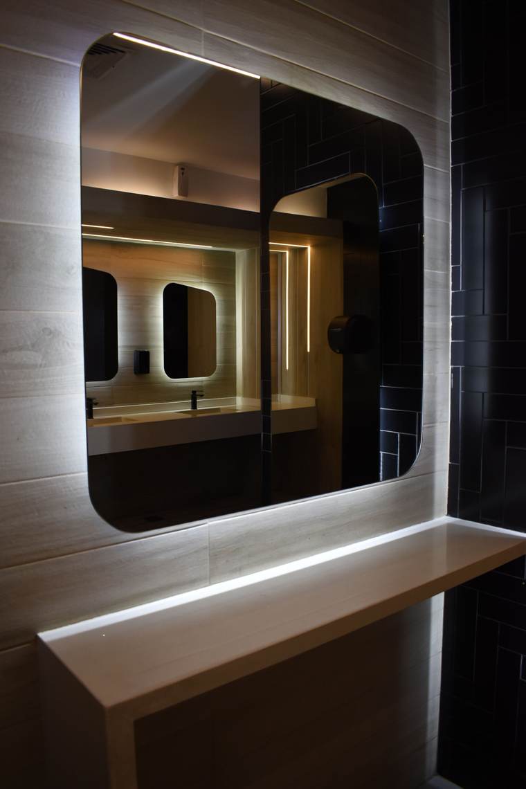 Modern restroom with backlit mirrors and dark wall tile