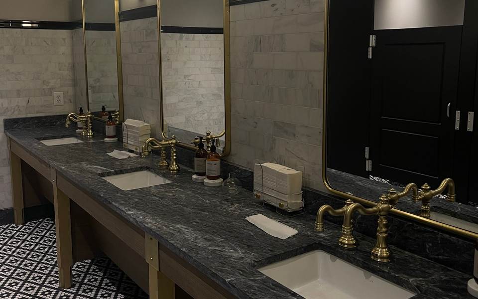 Commercial restroom with a black marble counter, brass faucets and tall framed mirrors
