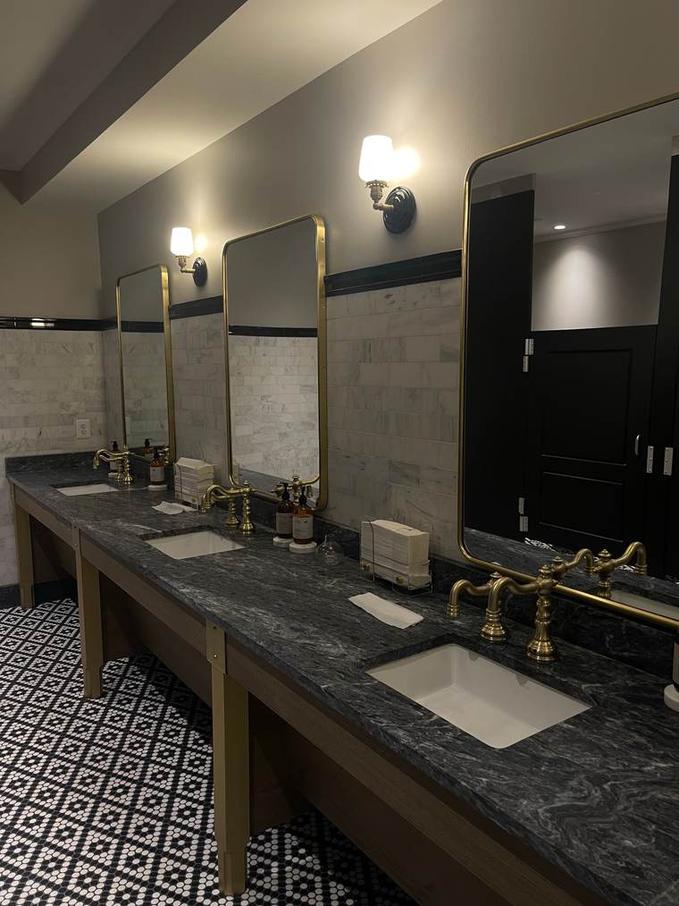 Restroom with a black marble counter, brass faucets and brass-framed mirrors