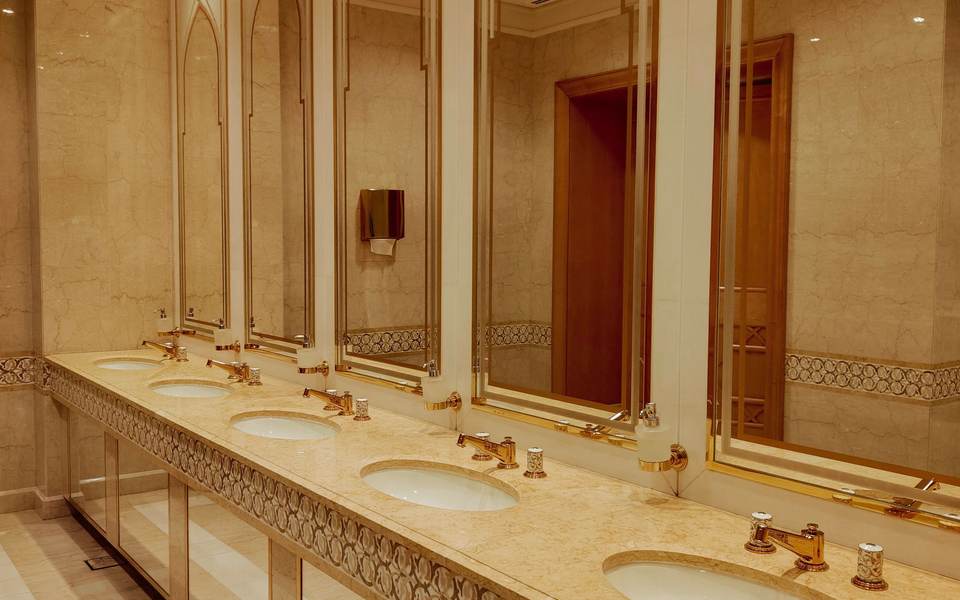 Commercial restroom with a long marble counter, round sinks and arched gold mirrors
