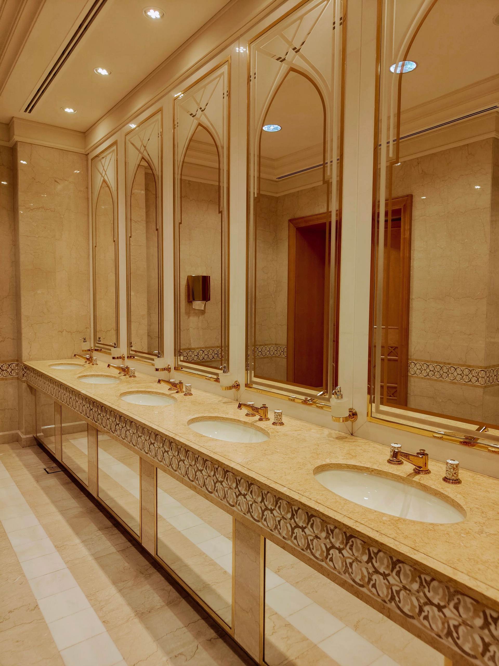 Commercial restroom with a long marble counter, brass faucets and arched mirrors