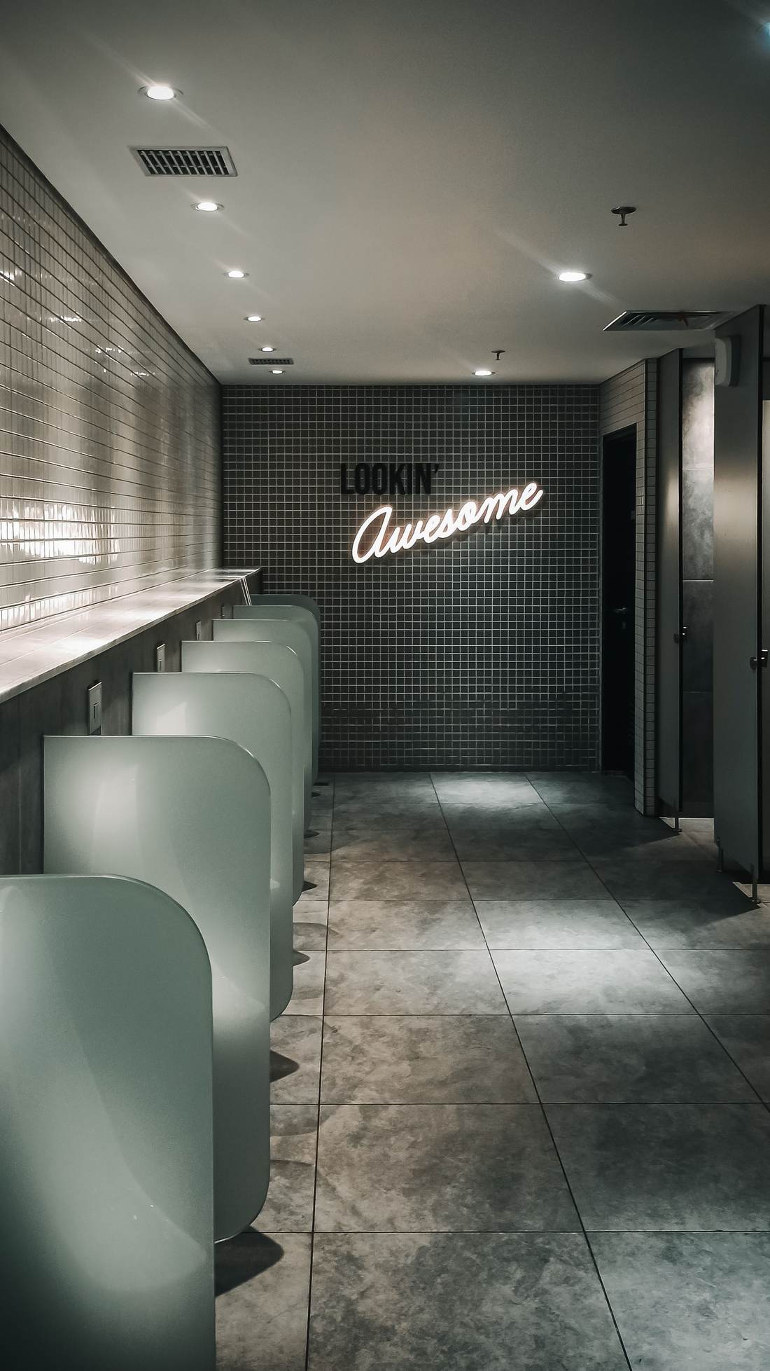 Restroom with dark green subway tile, wall-hung urinals and privacy dividers