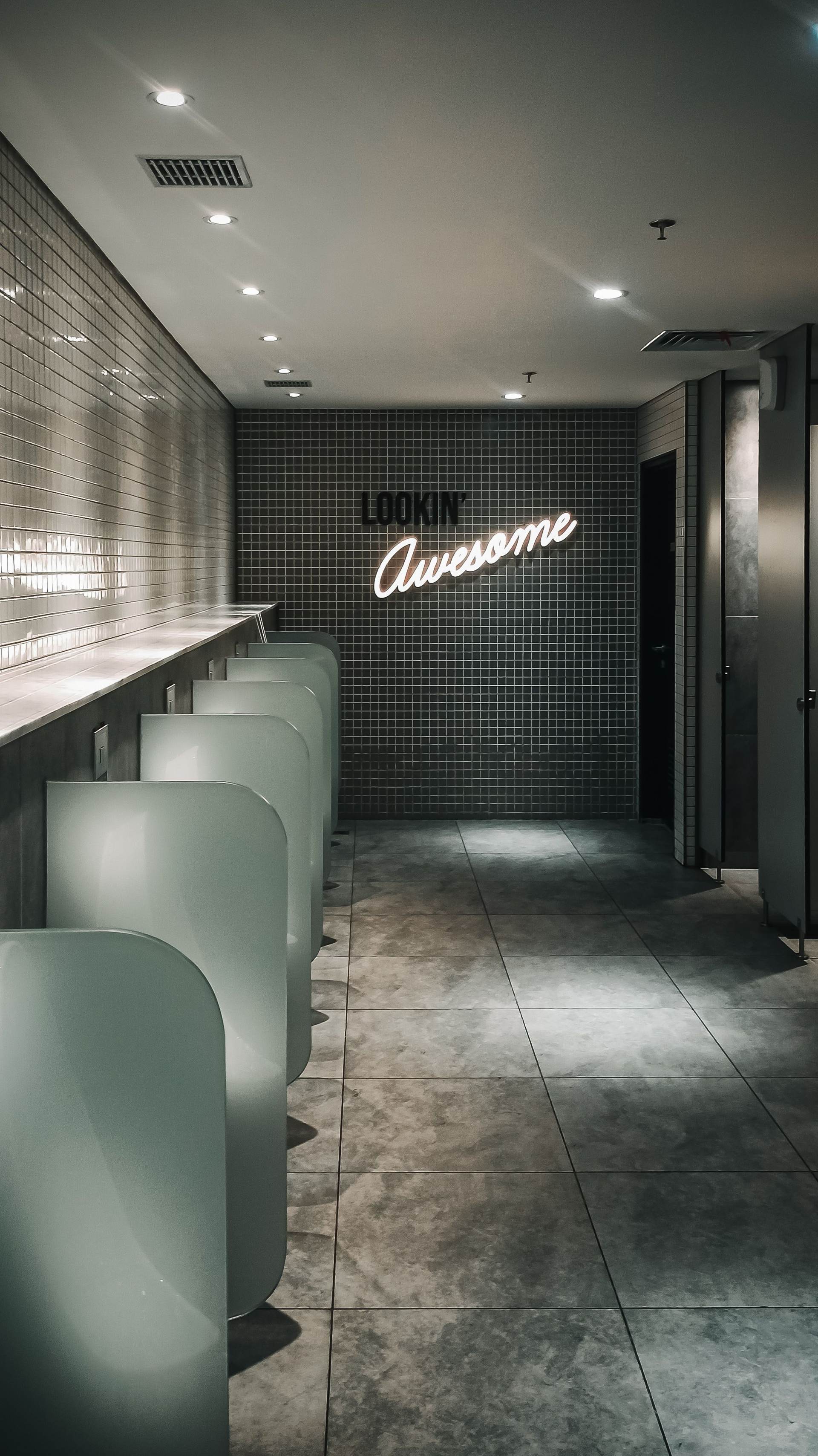 Commercial restroom with dark green subway tile walls, urinal dividers and toilet partitions