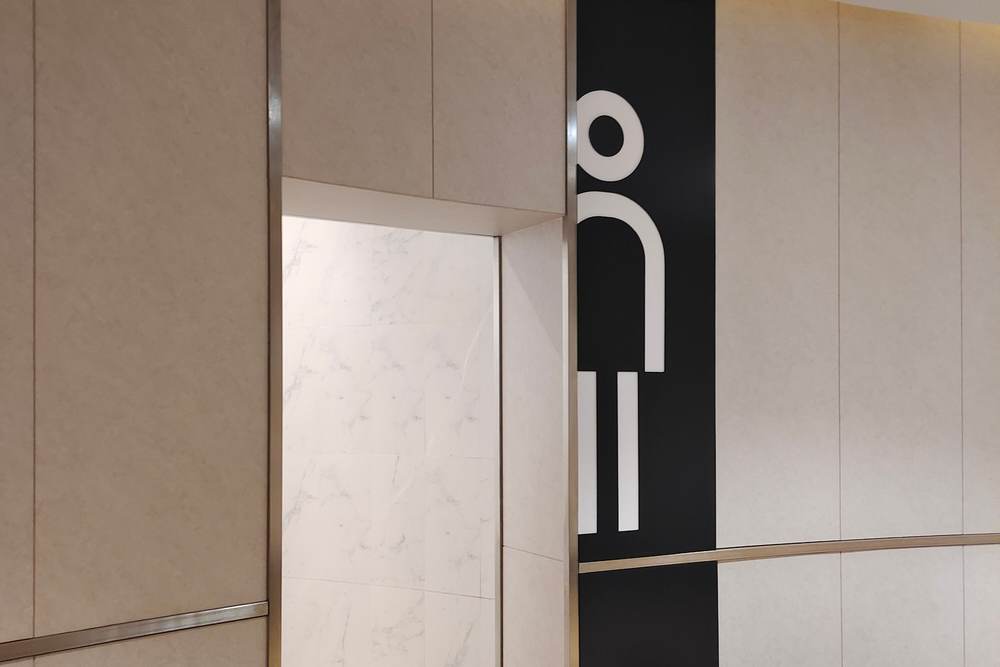 Modern restroom entrance with a large figure sign on a dark panel beside light marble-look walls
