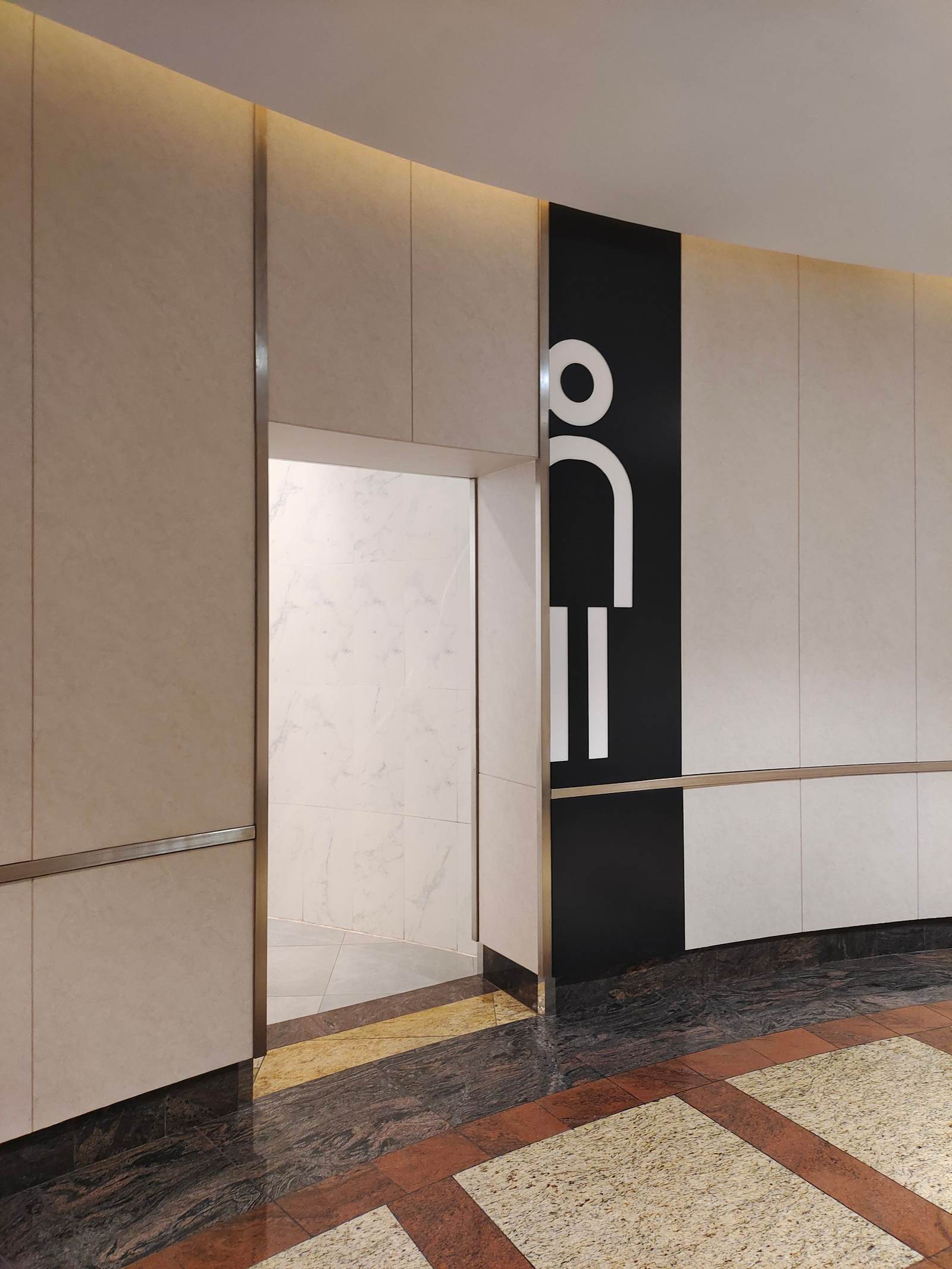 Modern restroom entrance with a large figure sign on a dark panel beside light marble-look walls