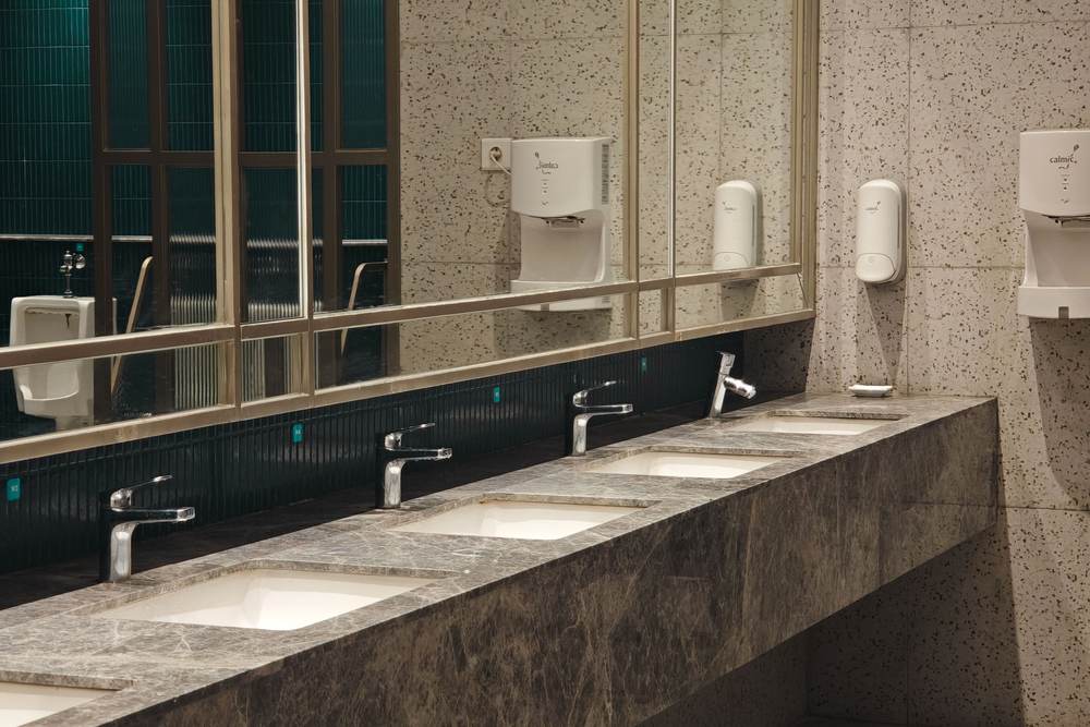 Commercial restroom counter in dark granite with undermount sinks, sensor faucets and a long mirror