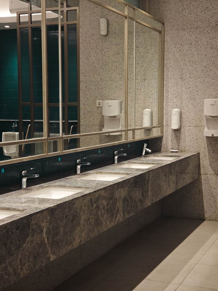Commercial restroom counter in dark granite with undermount sinks, sensor faucets and a long mirror