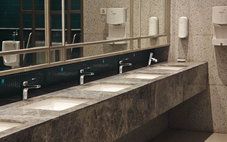 Commercial restroom counter in dark granite with undermount sinks, sensor faucets and a long mirror