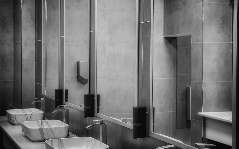 Commercial restroom with gray tile walls and a row of vessel sinks under mirrors
