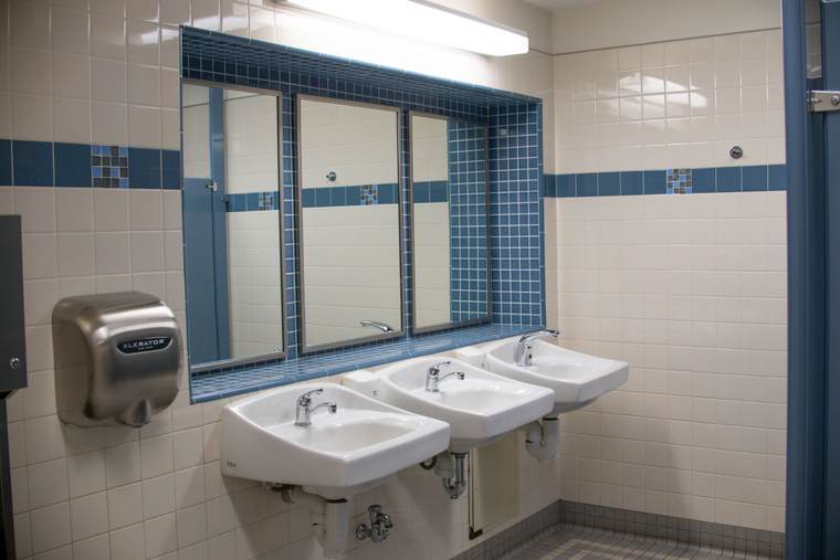 Public restroom with three wall-hung sinks under a window and a stainless hand dryer on white tile